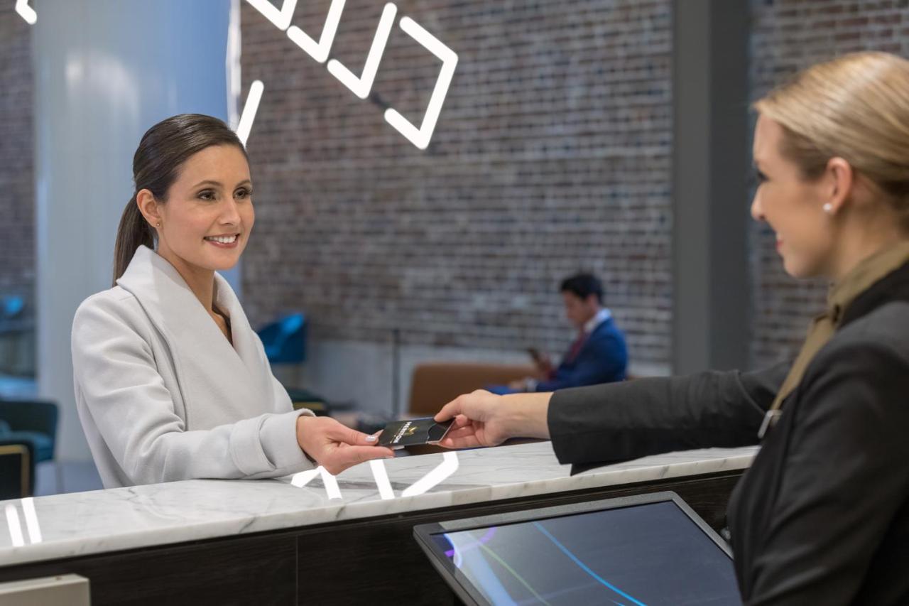 Meriton Suites Sussex Street, Sydney Exterior foto The image depicts a scene at a hotel reception desk. A woman with long hair, dressed in a white outfit, is smiling as she hands her card to a receptionist, who is in a black uniform. The reception area features a modern design, and there is a person 