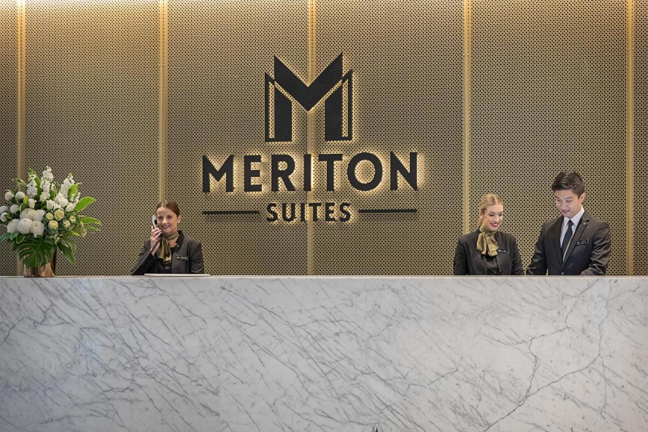 Meriton Suites Sussex Street, Sydney Exterior foto The photo depicts the reception area of a hotel called "Meriton Suites." In the background, there is a large, illuminated sign featuring the hotel’s logo. The reception desk is made of marble and is staffed by two individuals dressed in professional 